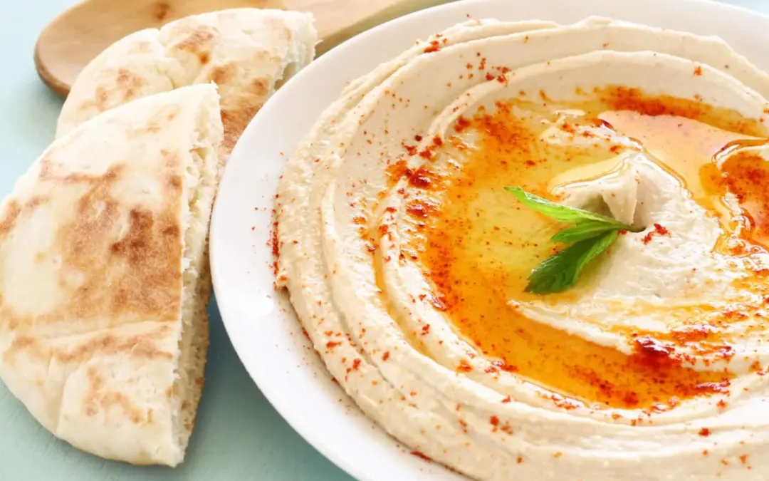 hummus served on a white plate with pita bread
