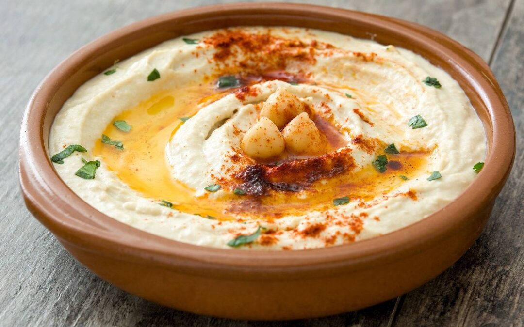 A bowl of creamy hummus garnished with a single swirl on top, presented on a wooden table