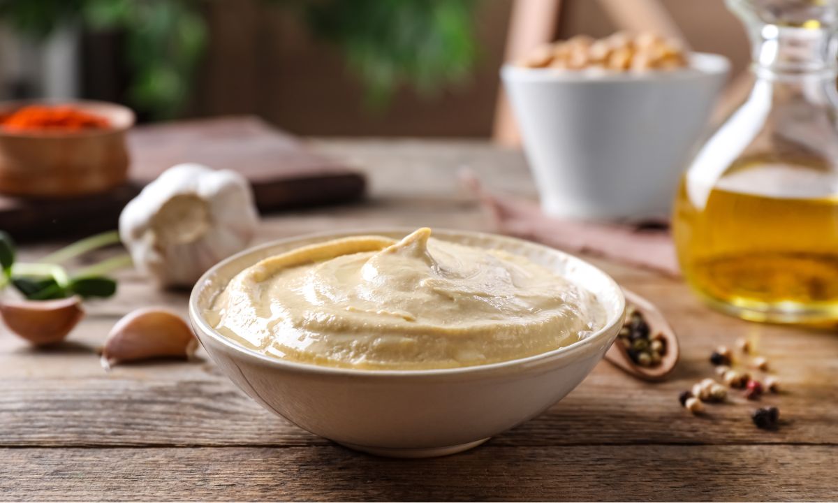 A bowl of creamy hummus garnished with a single swirl on top, presented on a rustic wooden table