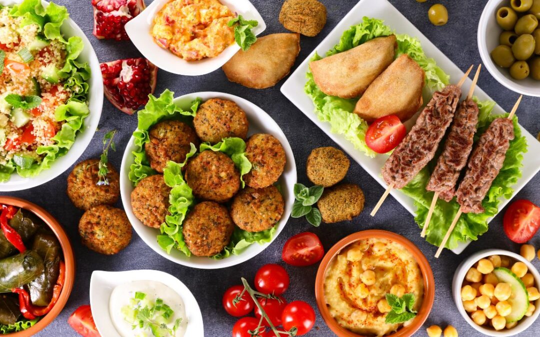 An assortment of Mediterranean diet dishes displayed on a table, including falafel, stuffed grape leaves, grilled meat skewers, various dips like hummus and tzatziki, fresh salad with quinoa, and ripe tomatoes, with a side of olives.