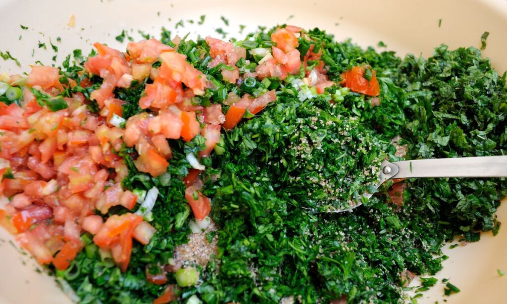 Ingredients for tabouli, with finely chopped parsley on one side and diced tomatoes and green onions on the other