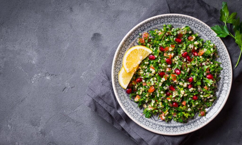 Tabouli garnished with pomegranate seeds served in a speckled ceramic bowl