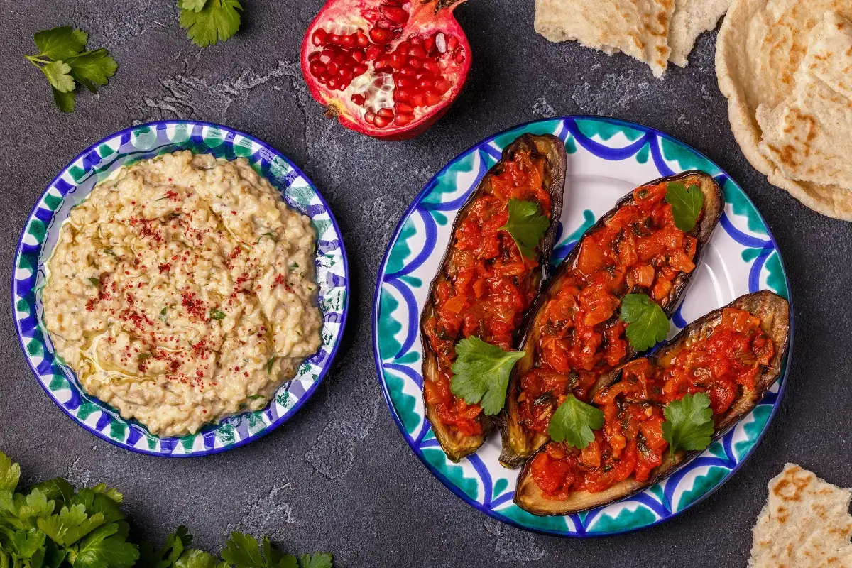 Gluten-free baba ganoush and roasted stuffed eggplants served with pomegranate, parsley, and flatbread on decorative plates