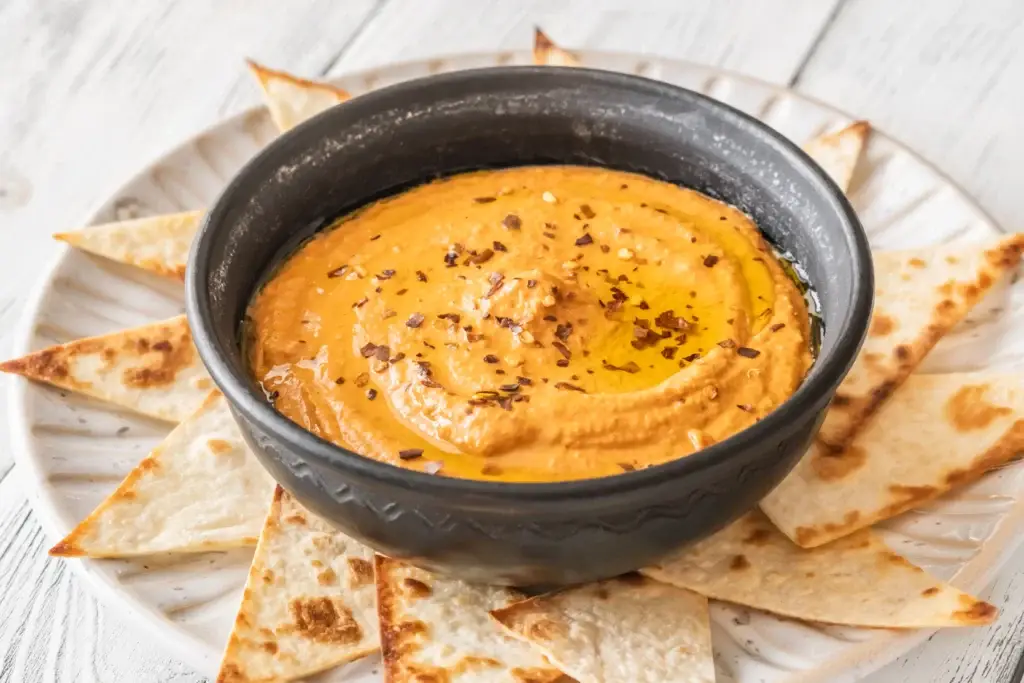 Classic muhammara dip with roasted red peppers, walnuts, and pomegranate molasses, garnished with fresh herbs, served at Aladdin Mediterranean Cuisine.