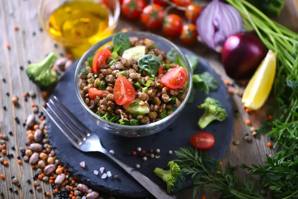 Fresh gluten-free lentil salad with cherry tomatoes, cucumber, spinach, and broccoli on a slate plate with colorful ingredients in the background