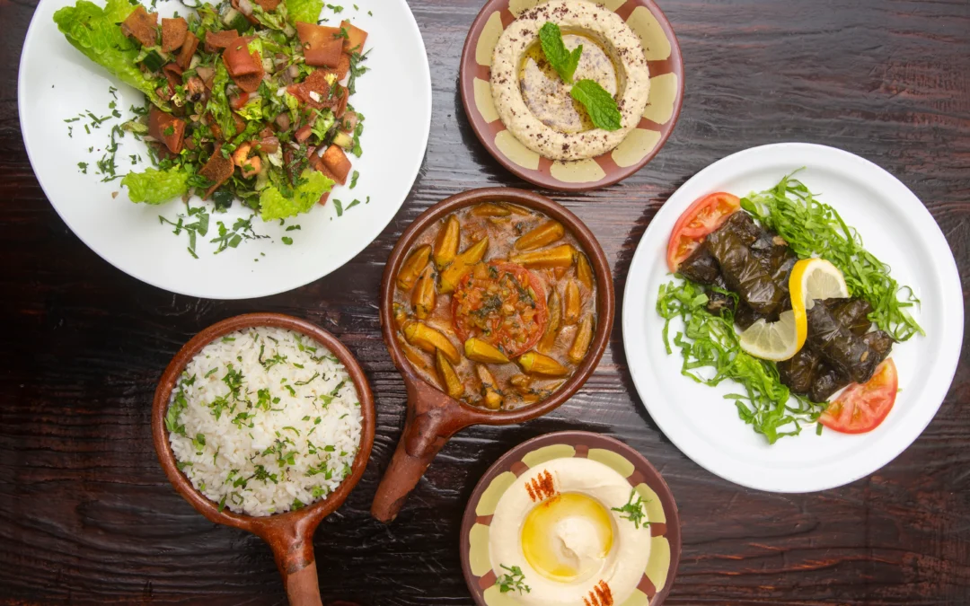 Traditional Mediterranean dishes including hummus with olive oil, fattoush salad, stuffed grape leaves with lemon, white rice, and okra stew served on a rustic table at Aladdin Mediterranean Cuisine.