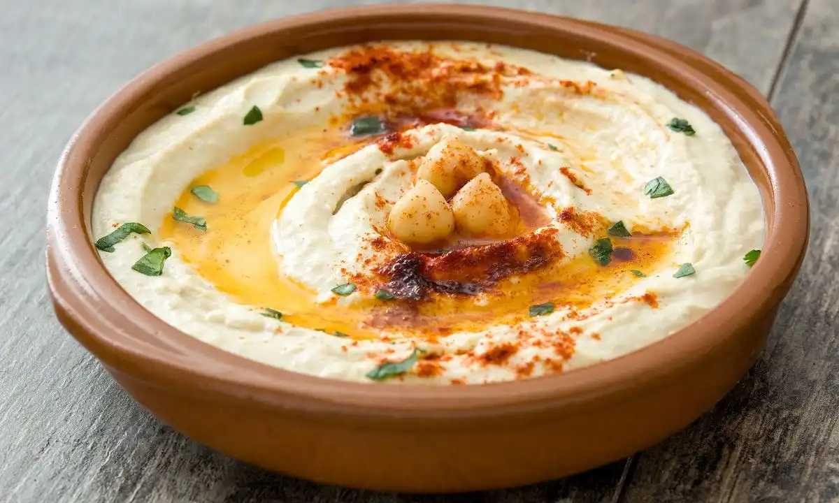 A bowl of creamy hummus garnished with a single swirl on top, presented on a wooden table