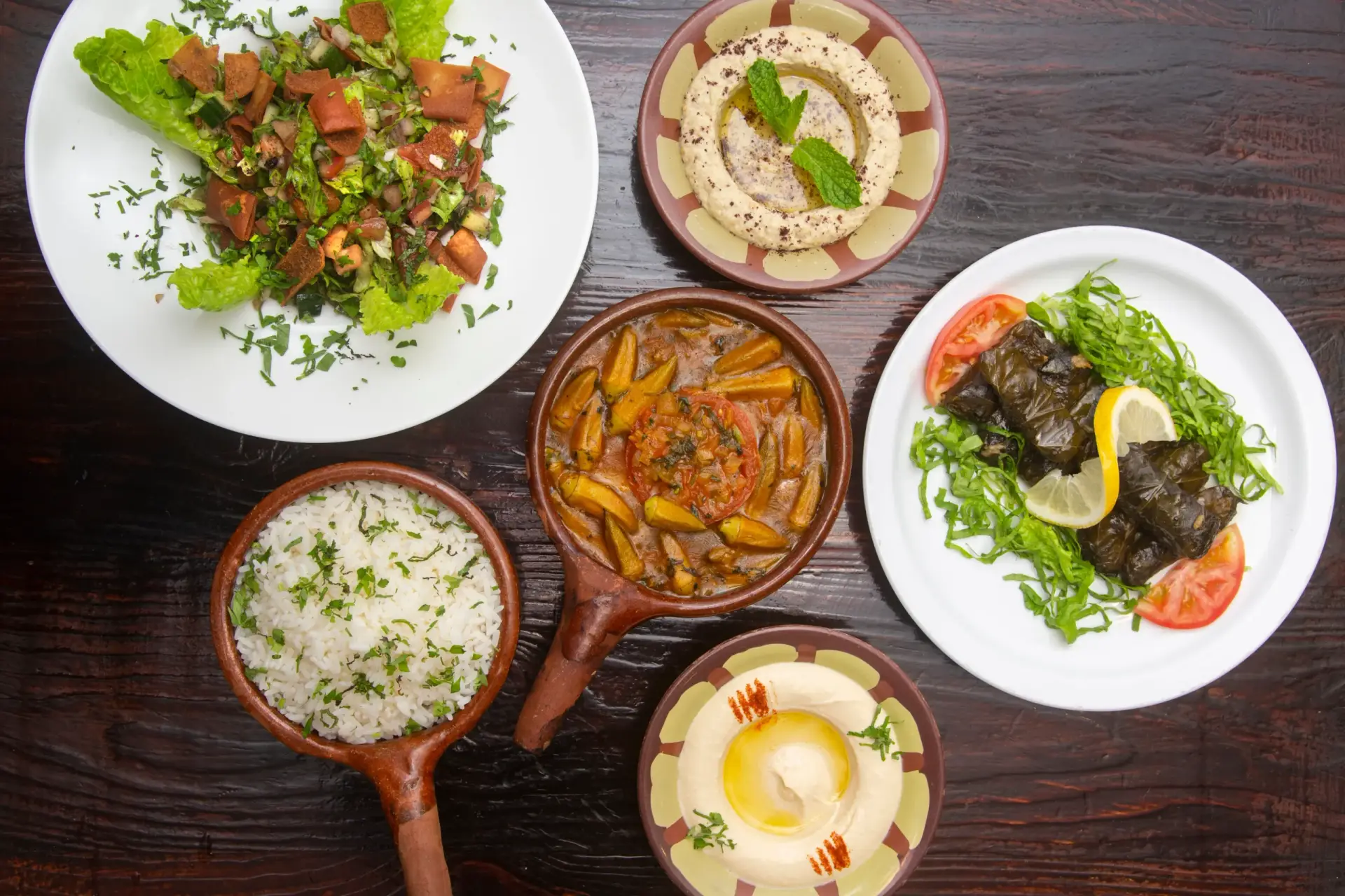 Traditional Mediterranean dishes including hummus with olive oil, fattoush salad, stuffed grape leaves with lemon, white rice, and okra stew served on a rustic table at Aladdin Mediterranean Cuisine.