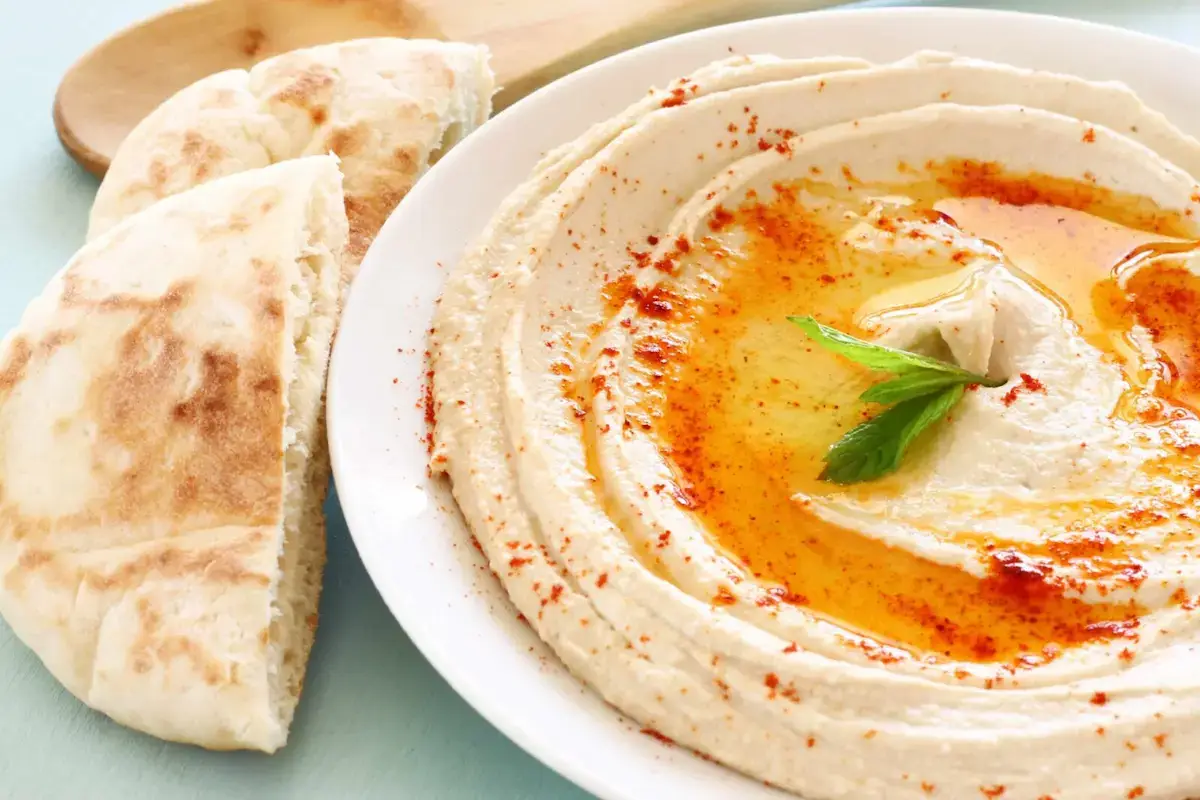 A plate of hummus drizzled with olive oil and sprinkled with cumin, served with pita bread