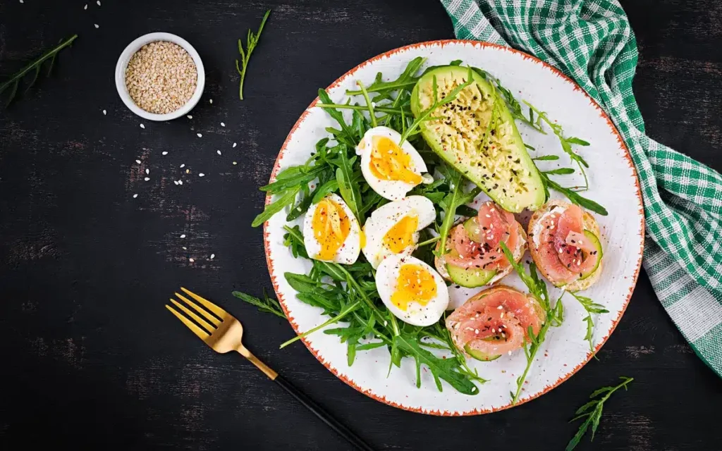 "Keto Mediterranean salad with arugula, avocado, boiled eggs, and smoked salmon, topped with sesame seeds.