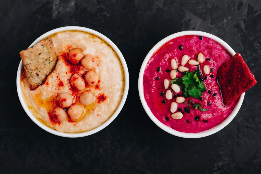 Classic hummus and vibrant beetroot hummus topped with pine nuts and herbs, highlighting the health benefits of Mediterranean food