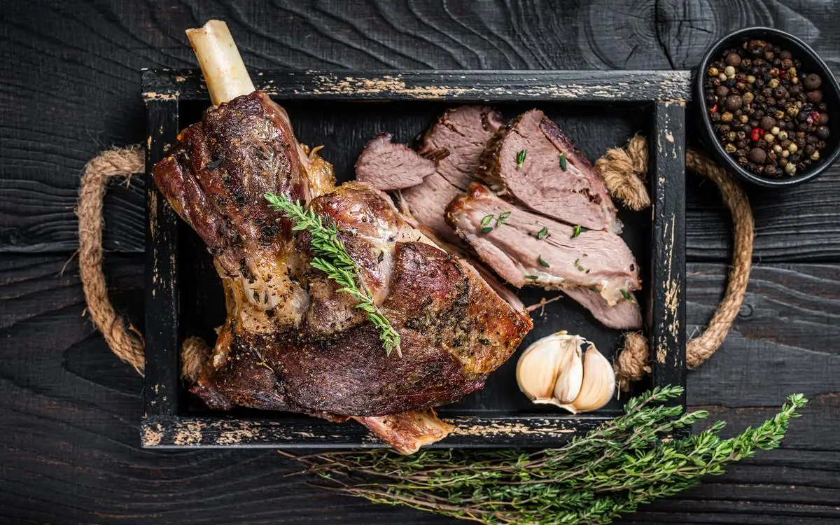 Mediterranean-style slow-roasted lamb leg sliced and served with garlic and herbs.