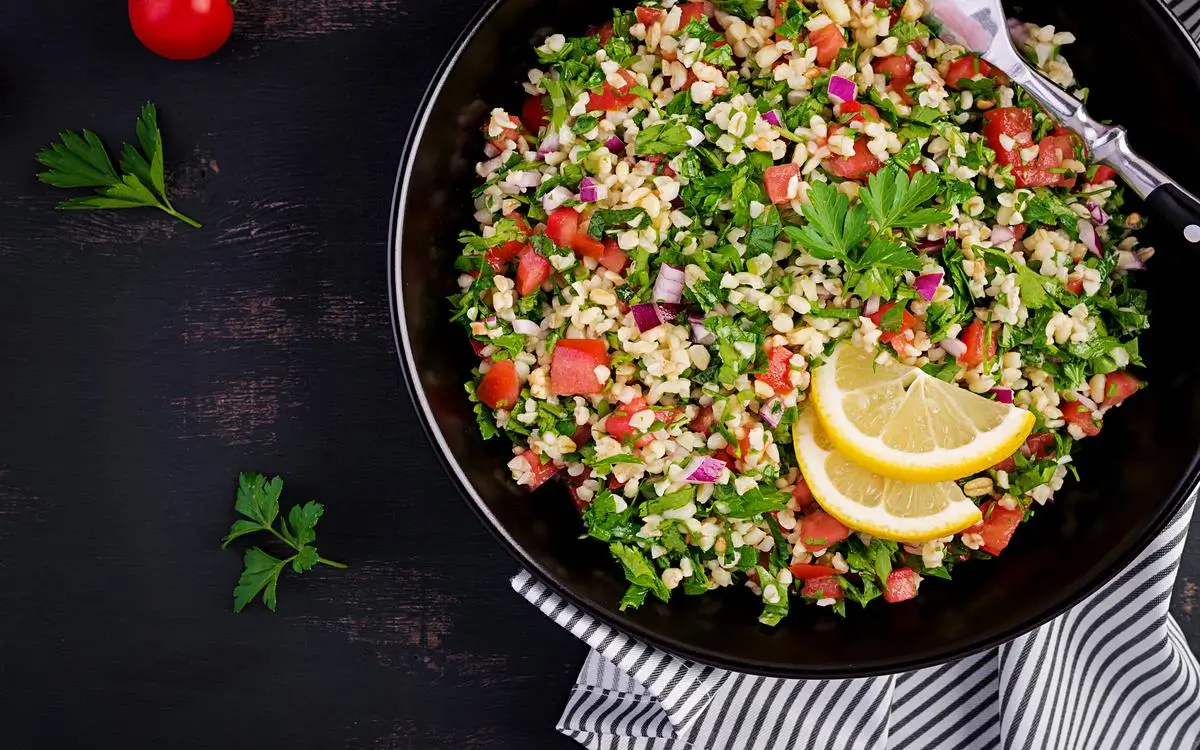 Vegan Mediterranean tabouli salad with chopped parsley, tomatoes, cucumbers, red onions, and lemon slices.