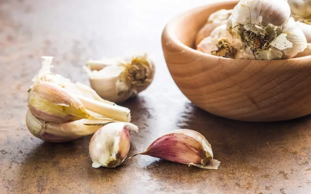 Fresh garlic cloves in a wooden bowl with peeled garlic pieces on a rustic kitchen counter for a toum recipe