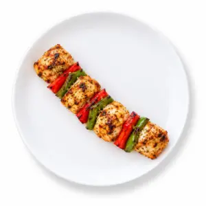 Grilled Mediterranean chicken kabob with red and green bell peppers on a white plate.